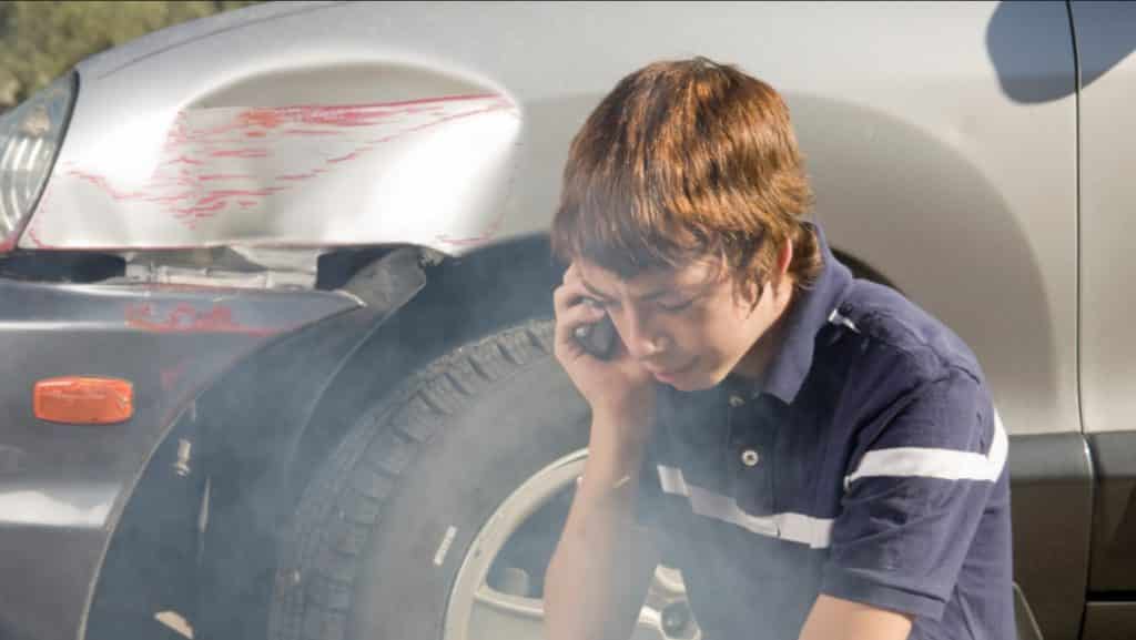 Teenager taling on the phone in front of a damaged vehicle