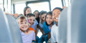 A group of smiling children sit and stand between the seats of a school bus, looking toward the camera, with sunlight streaming in—a perfect moment for Back-to-school bus safety: A Family Guide for Northland Kids & Parents.