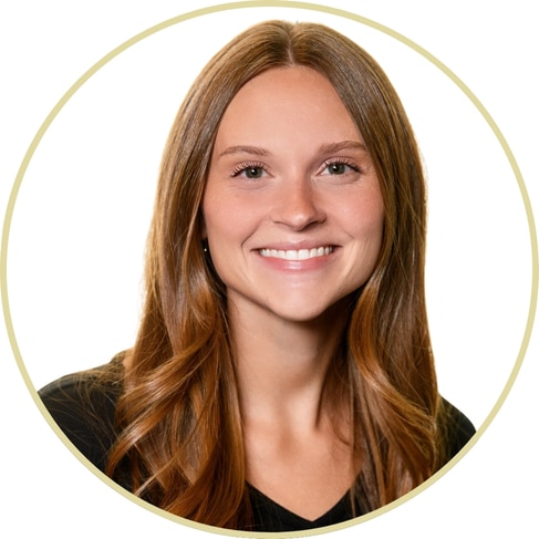 Adriana Wickett, a young woman with long, light brown hair and a friendly smile, is pictured wearing a black top against a white background within a circular frame.