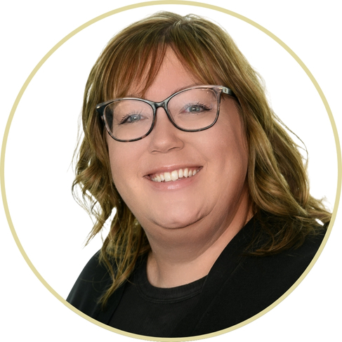 Adriana Wickett, a woman with light brown wavy hair, wearing glasses and a black top, smiles at the camera against a white background with a circular border.