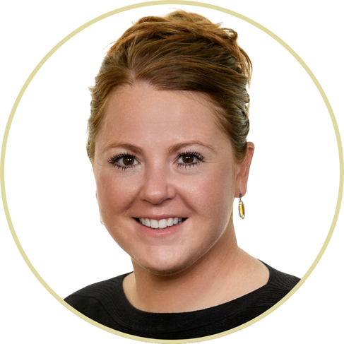Portrait of Adriana Wickett, a smiling woman with light skin and brown hair tied back, wearing a black top and a single dangling earring, shown against a white background within a circular frame.