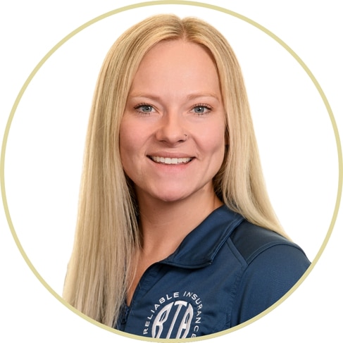 A woman with long straight blonde hair, Adriana Wickett, smiles at the camera. She is wearing a dark blue jacket with a white logo and is set against a white background framed by a light circular border.