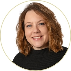 Becky Langlois, a woman with shoulder-length wavy light brown hair, wearing a black sweater, smiles at the camera against a white background with a thin circular border.