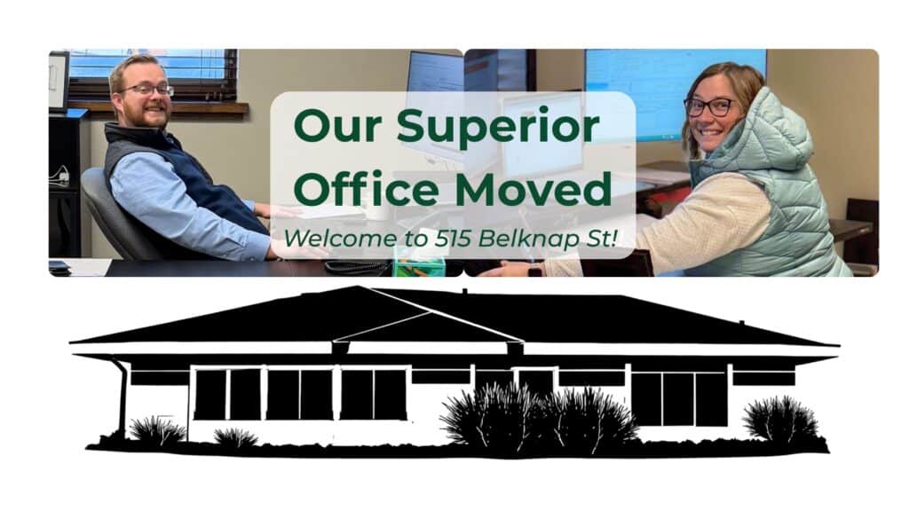 Two people smiling at desks in an office, with a sign that reads "Our Superior Office Moved. Welcome to 515 Belknap St!" Below is a black silhouette illustration of a building with shrubs in front.