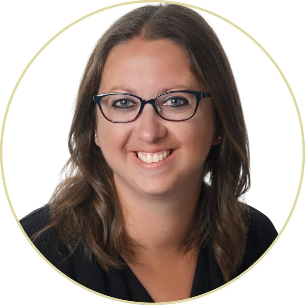 Woman with brown hair and glasses smiling, wearing a black top, on a white background.