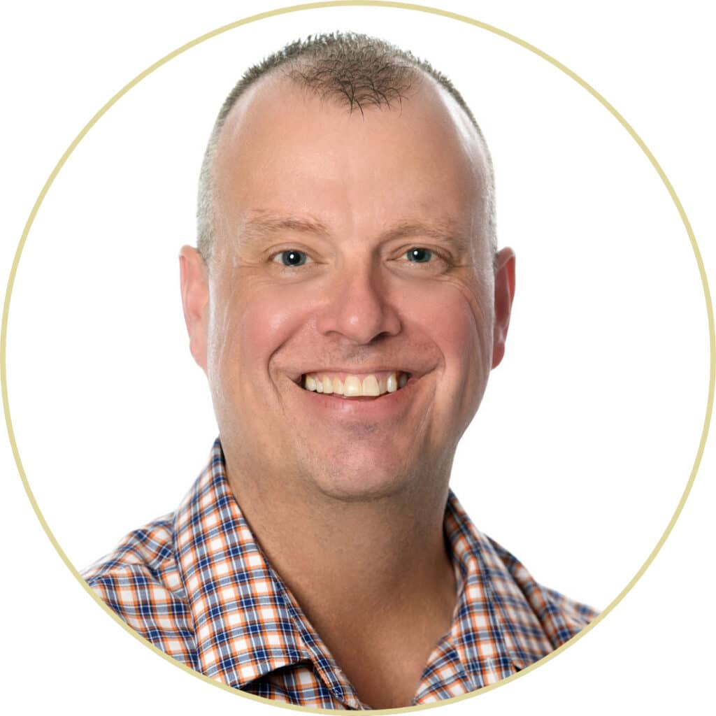 Headshot of a smiling man wearing a plaid button-down shirt.